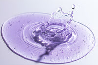 Nexa Serum droplet creating a circular splash on a reflective surface with a purple tint.